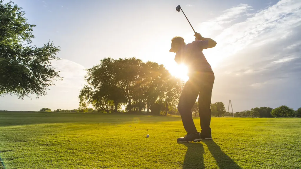 Golfer swinging while the sun rises behind him.